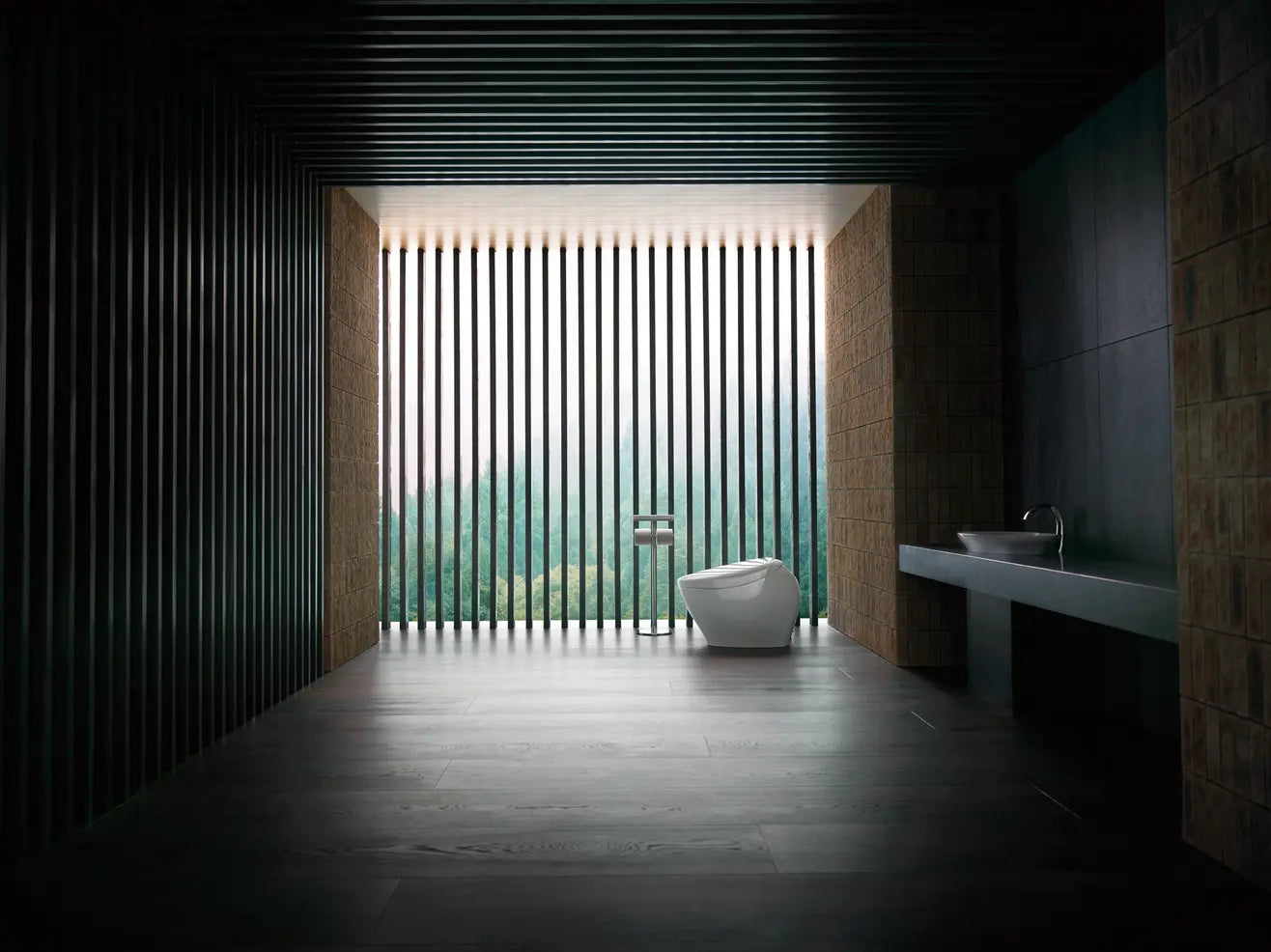A modern white toilet bowl with a wall-mounted faucet in a dark, minimalist bathroom with vertical slats and a sink on the right.