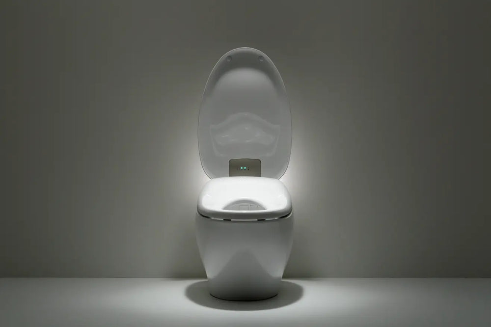 A white Neorest nx2 smart toilet with its lid open, illuminated by a built-in light on the seat. The toilet is centered against a dark gray background with the light casting a soft glow on the floor.