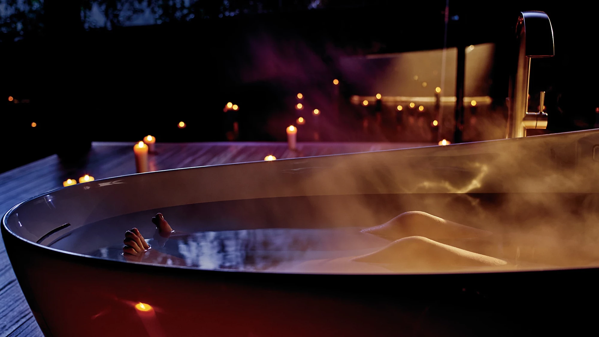TOTO Flotation Tub With ZERO DIMENSION - Person relaxing in a hot tub with candles lit around at night