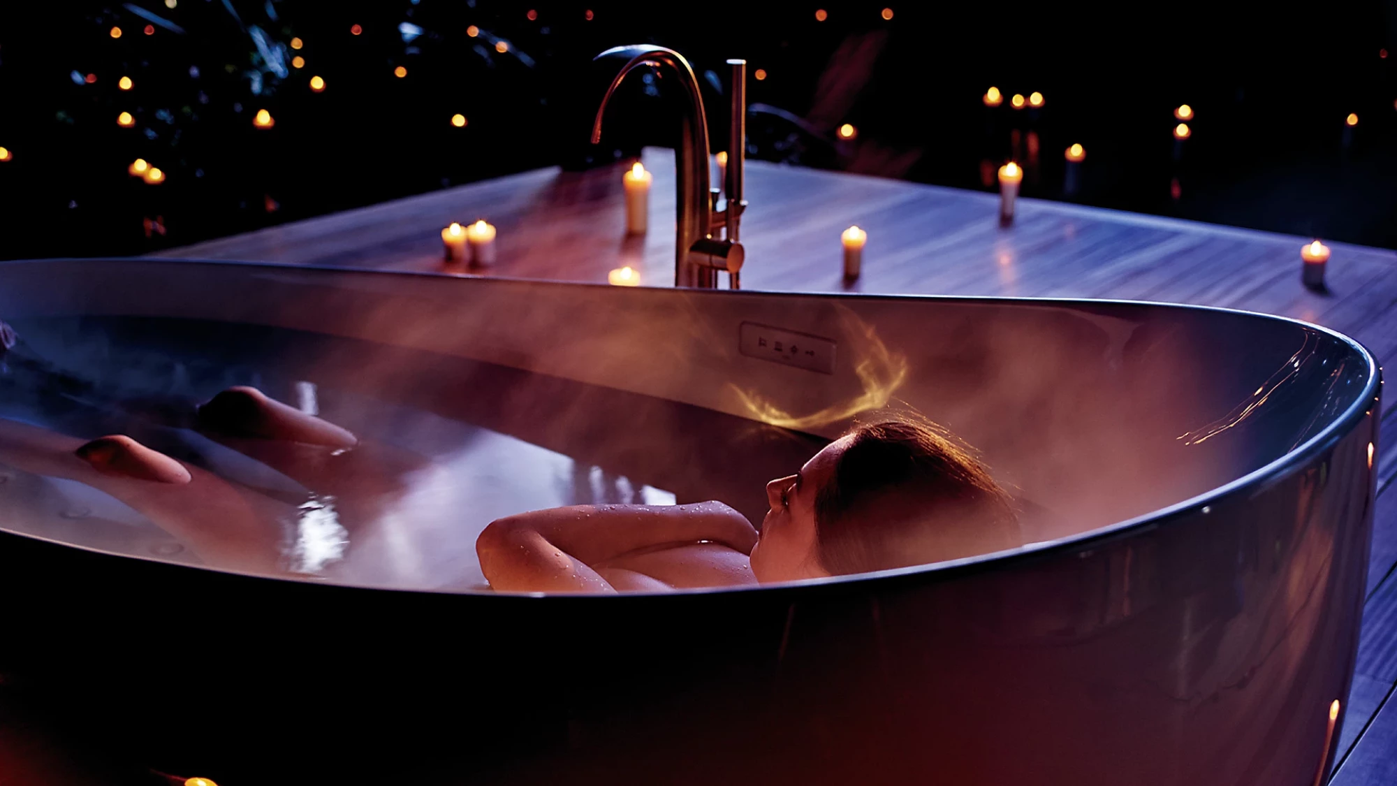 TOTO Flotation Tub With ZERO DIMENSION - Person relaxing in a steaming bathtub with candles around at night