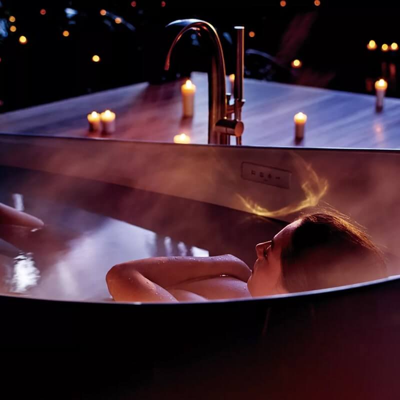 Woman relaxing in TOTO Flotation Tub with Zero Dimension, surrounded by candles, creating a serene and luxurious bathing experience.